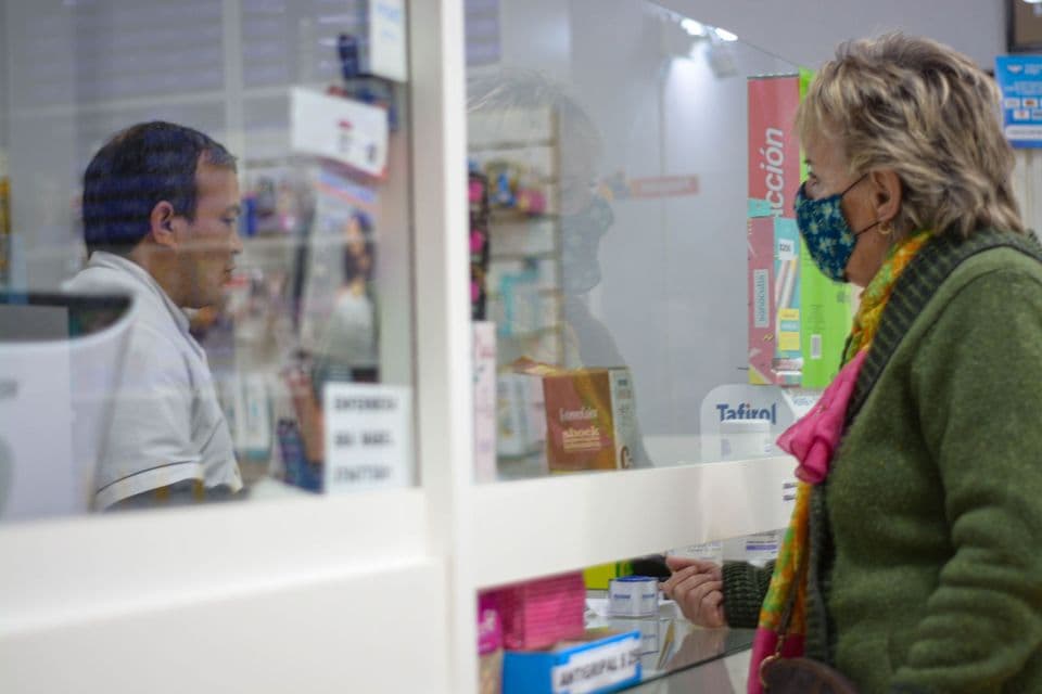 A customer wearing a face mask speaks with a pharmacist through a protective screen at the counter.